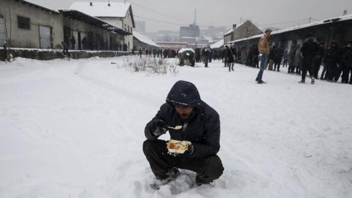 Un refugiado come en medio de la nieve en Belgrado.-REUTERS / MARKO DJURICA