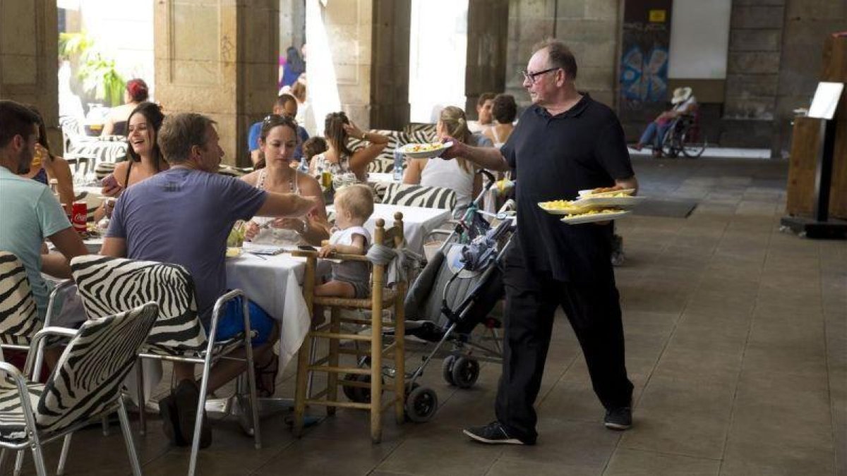 Un camarero sirve a un grupo de clientes en una terraza.-JOSEP GARCÍA