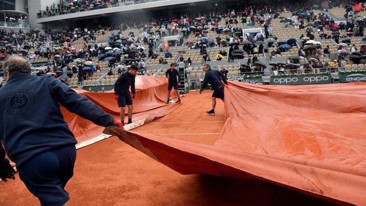 Varios operarios cubren con una lona la pista Philippe Chatrier donde jugaban Djokovic y Thiem.-EFE / JULIEN DE ROSA