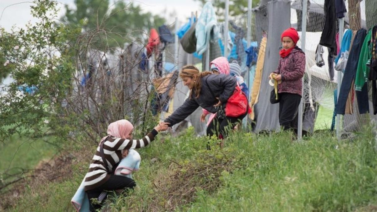 Una refugiada con su bebé en brazos, ayudada por otra a subir una colina en un campo cerca de Idomeni (Grecia), este miércoles.-AFP / TOBIAS SCHWARZ