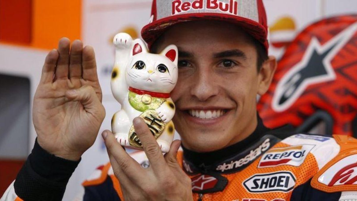 Marc Márquez muestra a su gato de la suerte japonés, al que tiene junto a él en el box del equipo Repsol Honda, en Motegi (Japón).-REPSOL MEDIA / JJAIME OLIVARES
