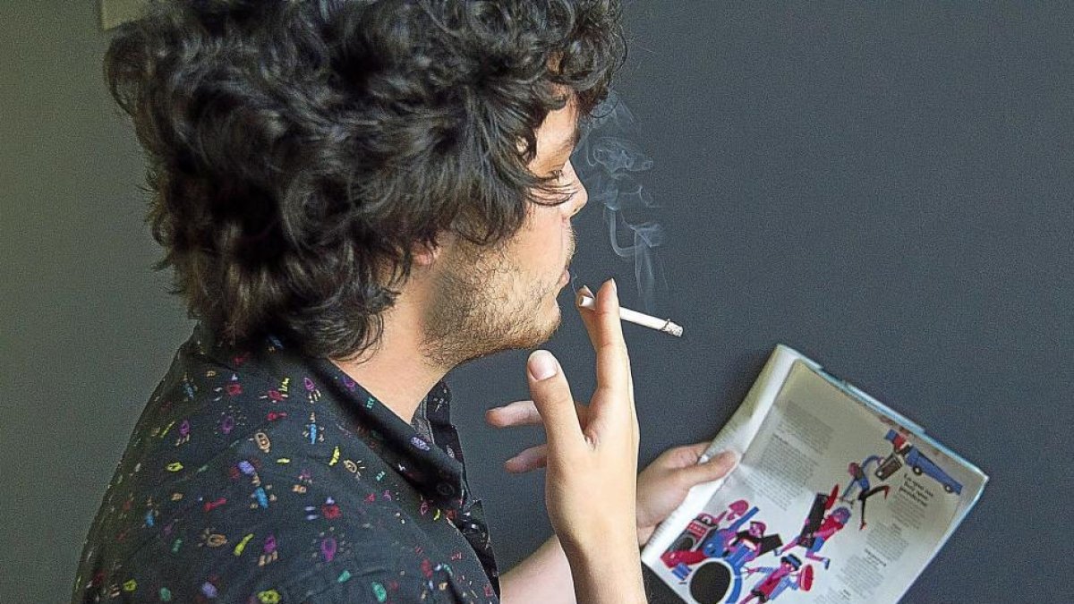 Un joven fuma un cigarrillo mientras lee una revista en Valladolid.-J. M. LOSTAU