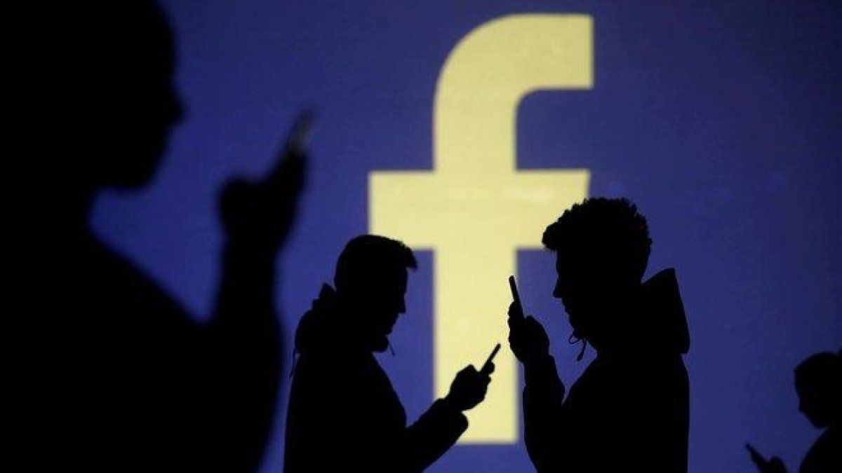 Usuarios de móvil ante el logo de Facebook.-