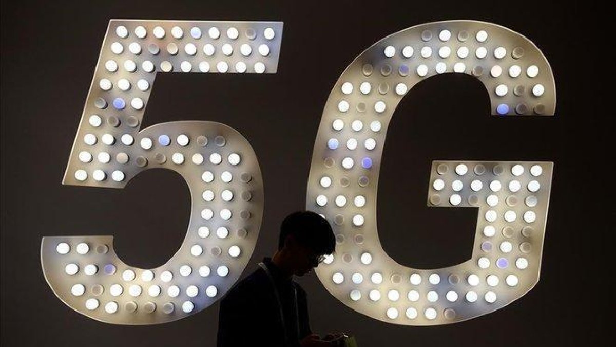 Un visitante usa su teléfono junto a un cartel de 5G en el estand de Intel.-JOSEP LAGO (AFP)