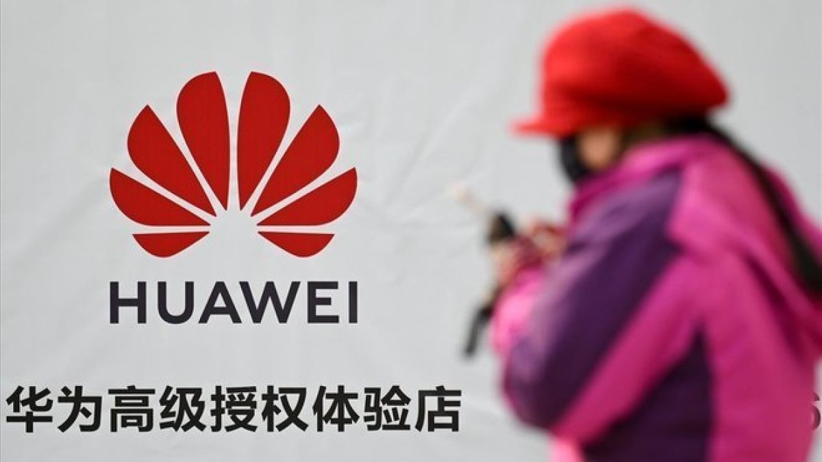 Una mujer consulta su smartphone junto a un cartel publicitario de Huawei, en una calle de Pekín.-WANG ZHAO (AFP)