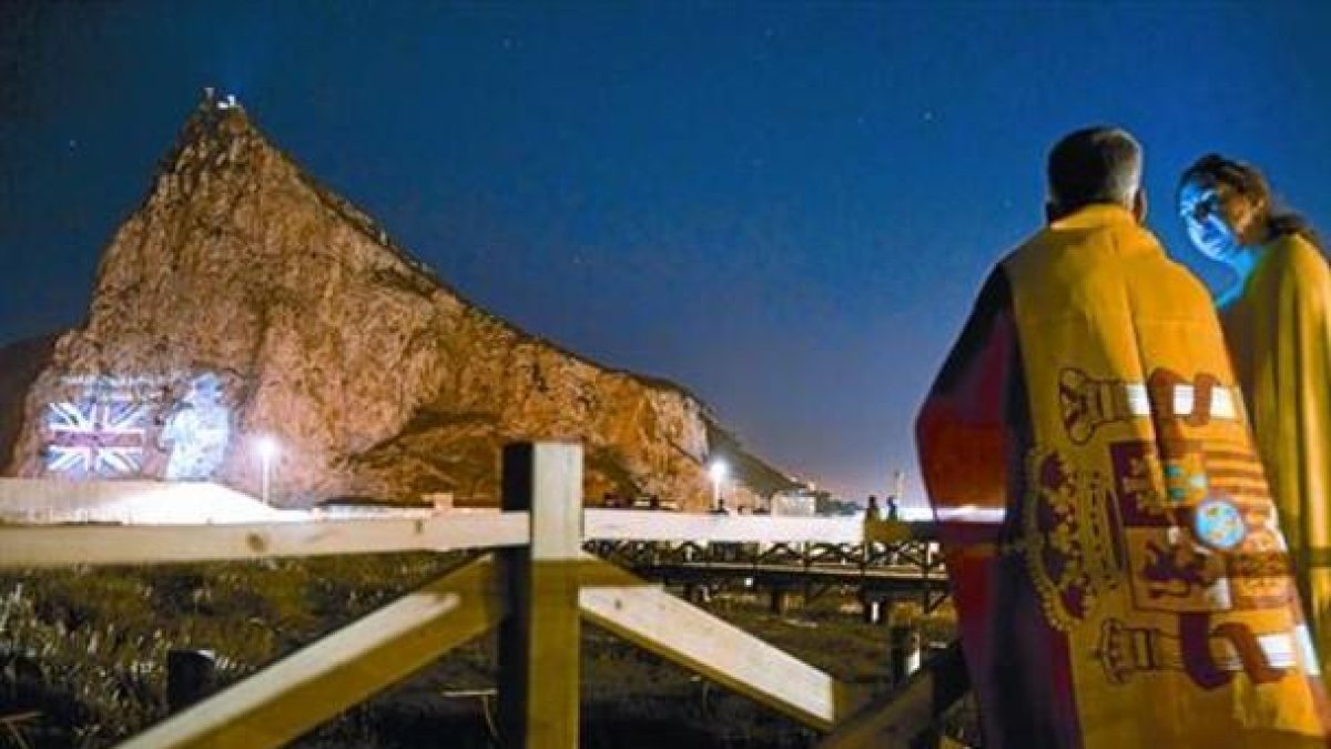 Una pareja mira desde la Línea de la Concepción la proyección de la imagen de Isabel II en el Peñón, en junio del 2012, cuando las autoridades de Gibraltar celebraron el 60º aniversario del ascenso al trono de la reina.-MARCOS MORENO