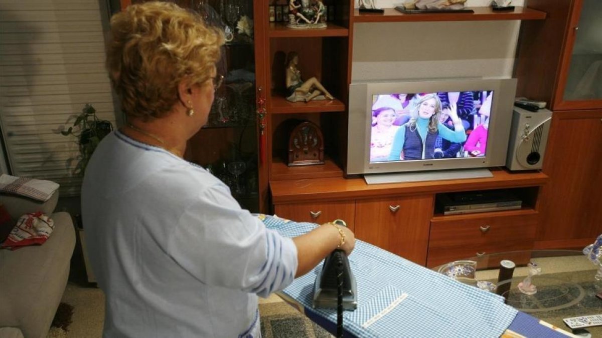 Ama de casa sigue un programa de televisión, mientras realiza labores del hogar.-FERRAN NADEU
