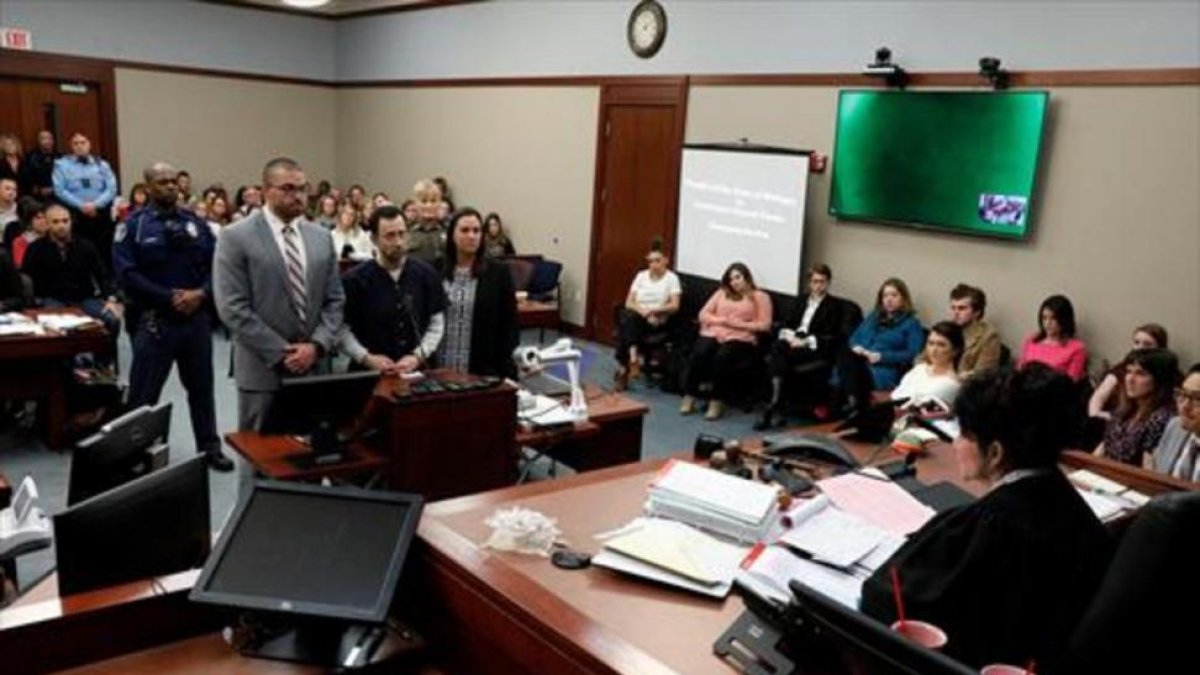 Larry Nassar, de pie, escucha la sentencia de la juez, ayer, en Michigan. Bajo esta foto algunas de sus víctimas.-/ REUTERS / MCDERMIN
