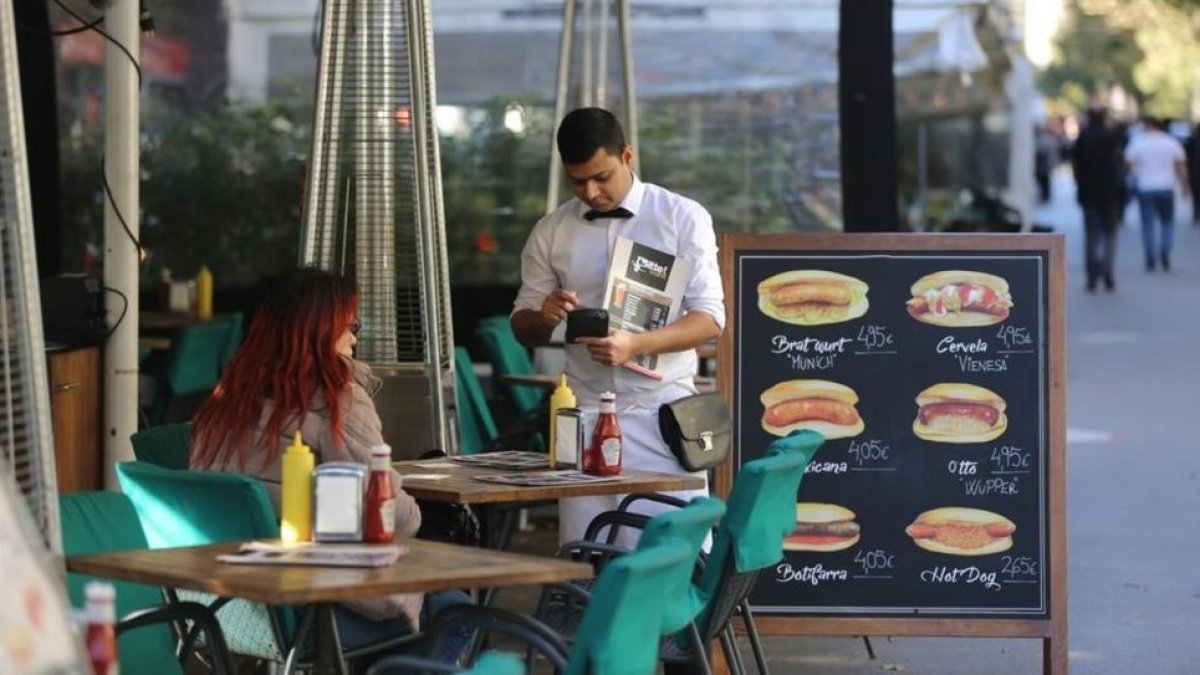 Un camarero sirve a unos clientes en una terraza.-DANNY CAMINAL