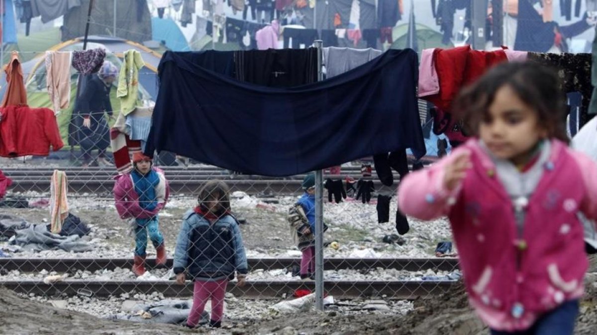 Niños refugiados juegan entre ropas colgadas para secar entre alambradas en un campo de refugiados de Idomeni (Grecia), junto a la frontera con Macedonia, este miércoles.-AP / BORIS GRDANOSKI
