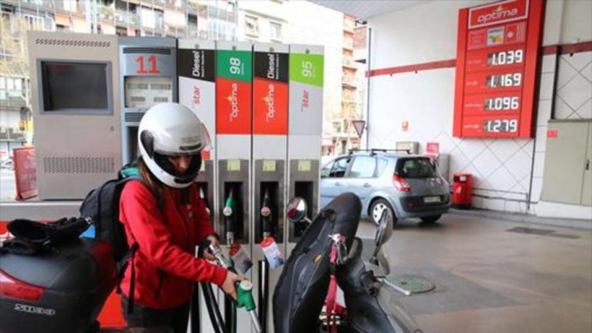 Una joven reposta carburante para su moto en una gasolinera-RICARD CUGAT