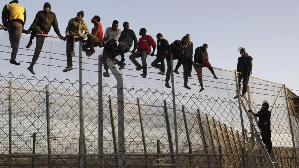 Policías españoles tratan de disuadir a inmigrantes encaramados a la valla de Melilla, fronteriza con Marruecos. /-EFE / ARCHIVO