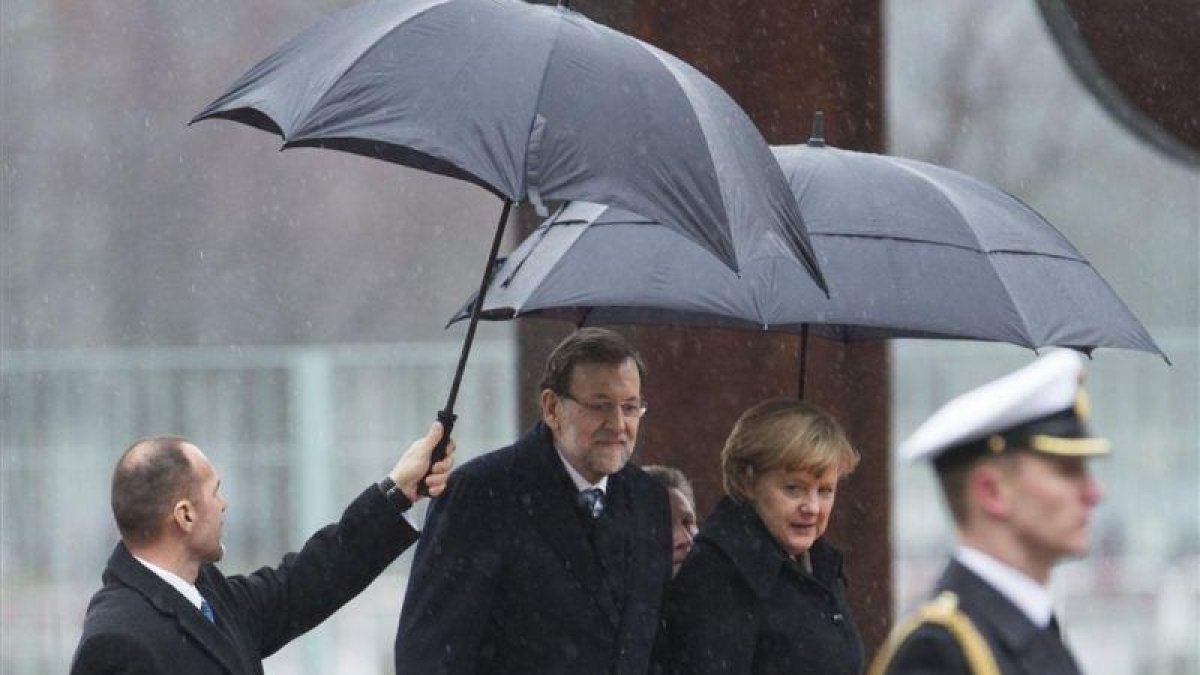 Mariano Rajoy y la cancillera alemana, Angela Merkel, en el 2013 en un día de lluvia en Berlín.-AP / GERO BRELOER