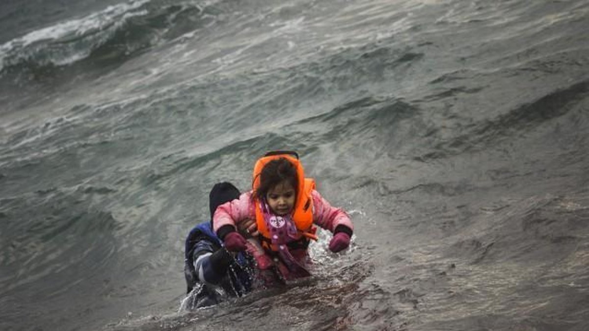 Un hombre ayuda a un niño cuyo barco ha naufragado este domingo en el Egeo.-AFP