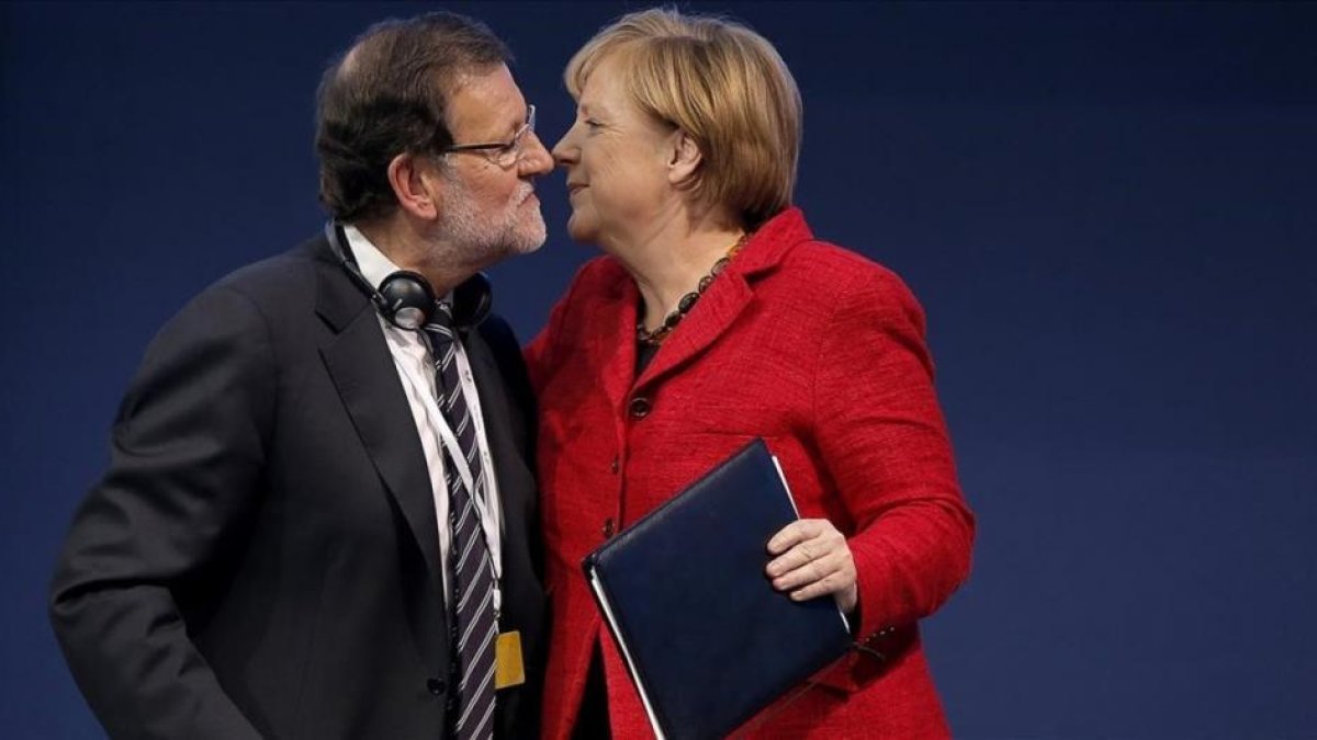 Rajoy y Merkel se saludan durante un congreso del Partido Popular Europeo.-EL PERIÓDICO