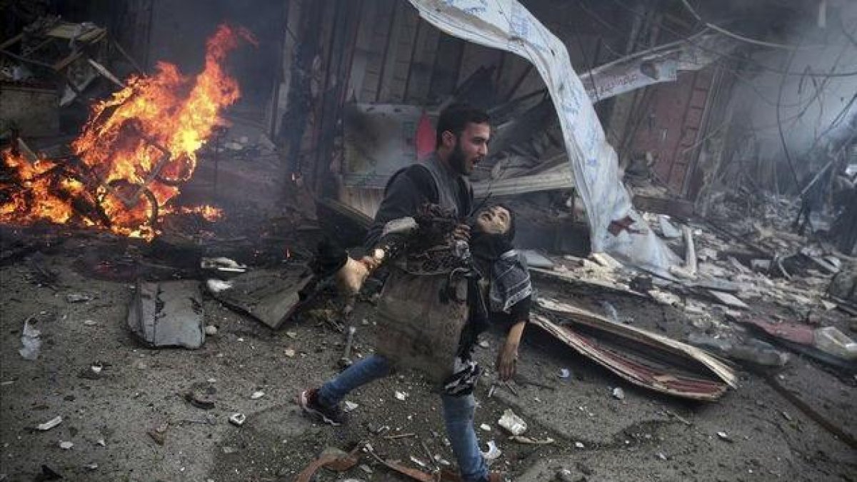 Un hombre sirio portando el cuerpo sin vida de un niño asesinado durante los bombardeos efectuados en la ciudad de Douma, Siria.-ABD DOUMANY