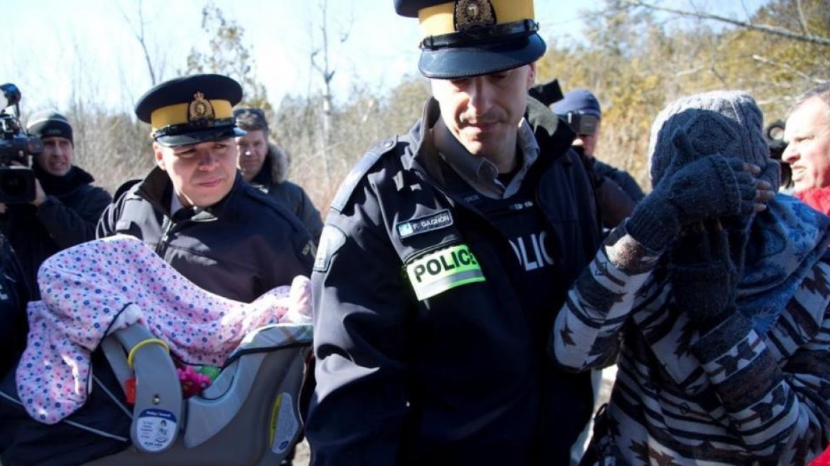 Una madre y su bebé escoltados por la policía montada de Canadá en la frontera de EEUU y Quebec.-CHRISTINNE MUSCHI