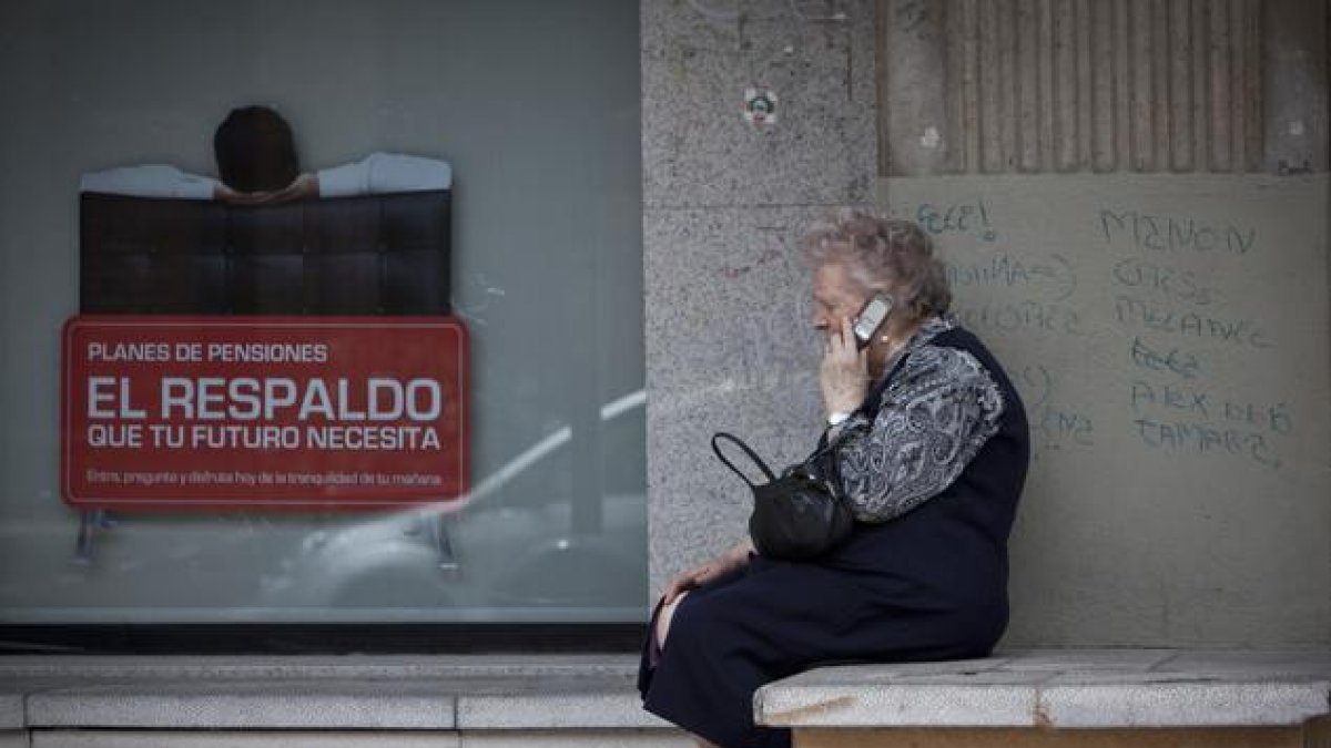Una mujer mayor habla por teléfono móvil al lado de un cartel de planes de pensiones.-MIGUEL LORENZO