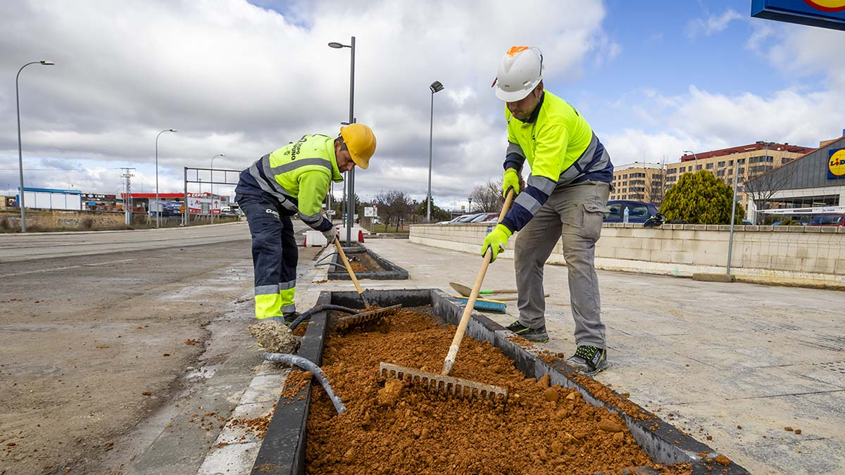 Dos operarios colocando la tierra en una de las jardineras instaladas en las nuevas aceras de Avenida de Valladolid.