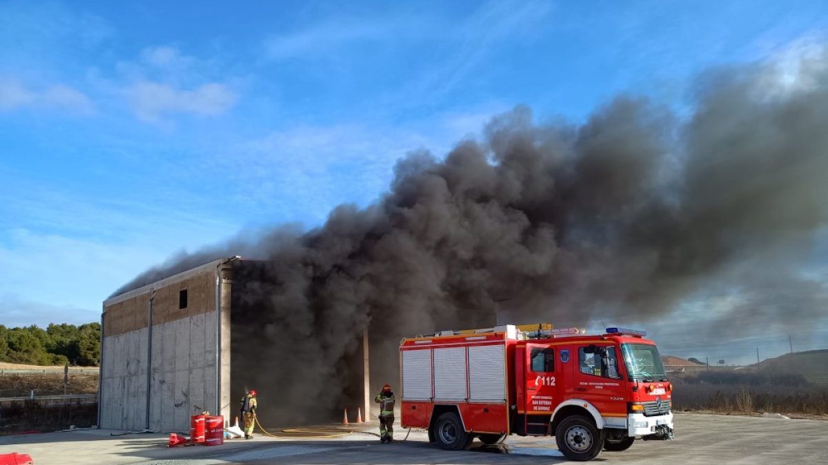 Los bomberos intervienen en la nave ante una densa humareda negra.