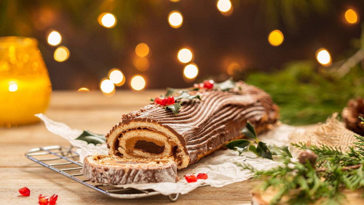 Tronco de Navidad decorado con chocolate, acebo y frutos rojos sobre mesa rústica navideña