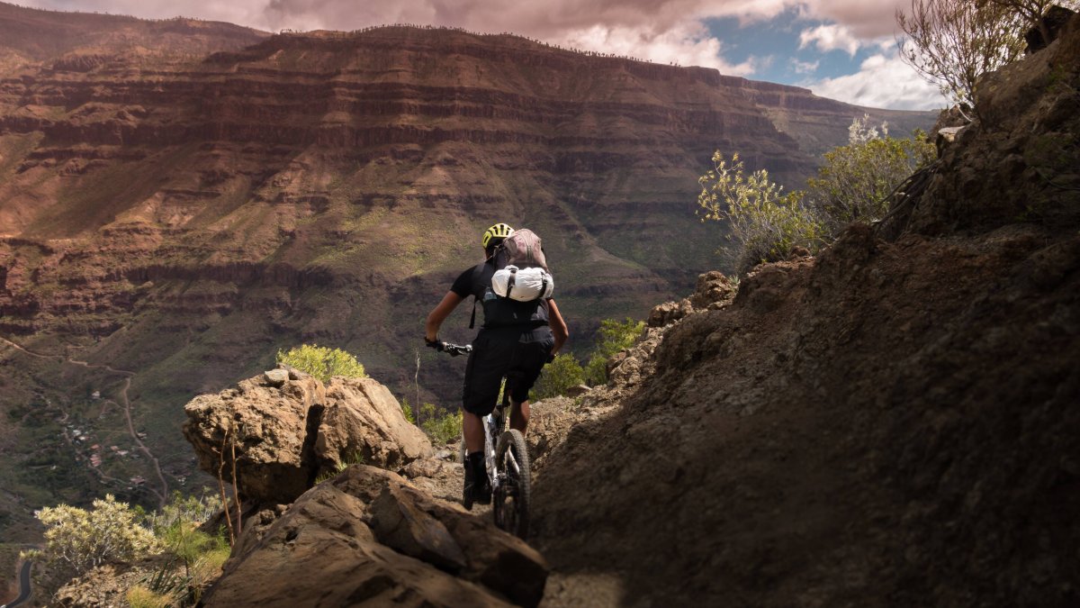Un ciclista de montaña atraviesa un sendero técnico rodeado de montañas y formaciones rocosas