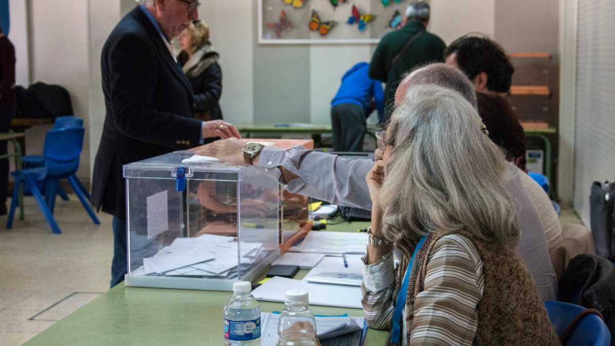 Un ciudadano introduce su voto en la urna mientras los miembros de la mesa electoral supervisan el proceso durante la jornada de votación