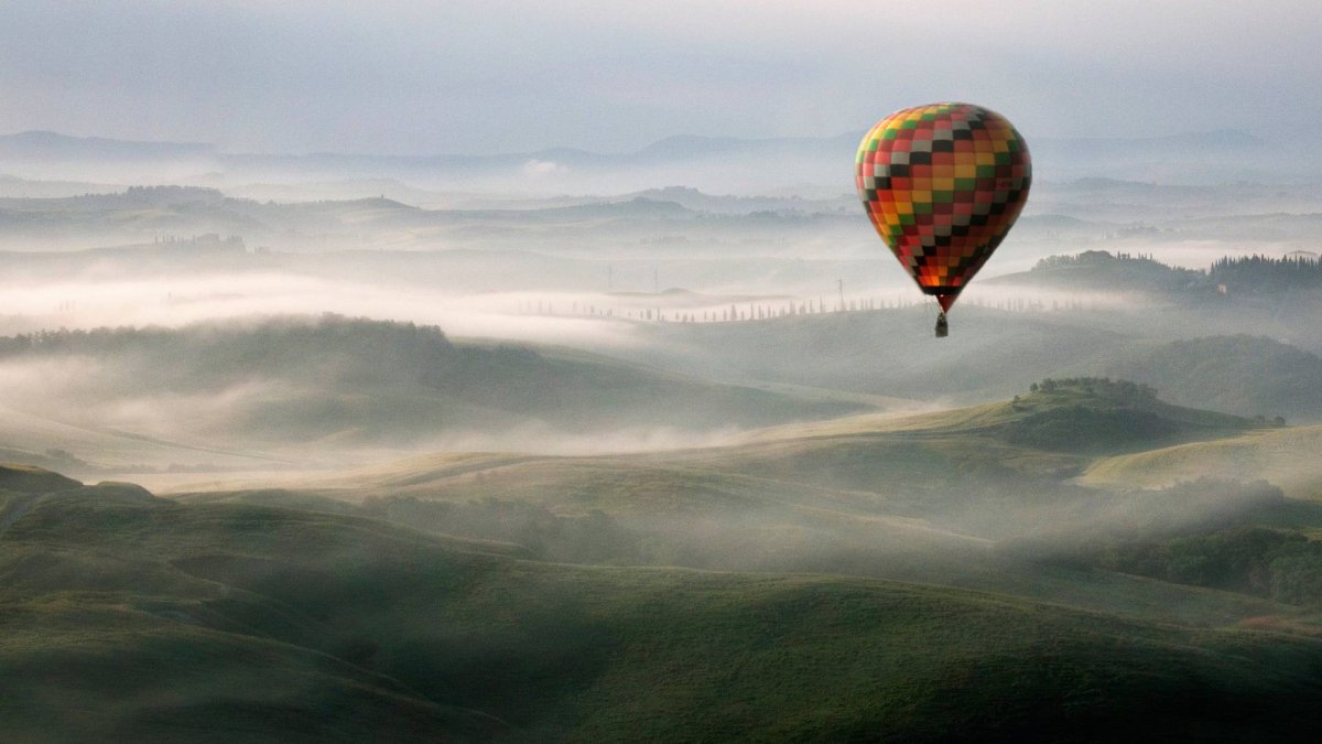 Un globo aerostático surca el cielo sobre un paisaje envuelto en niebla, evocando la experiencia única de contemplar el eclipse desde las alturas