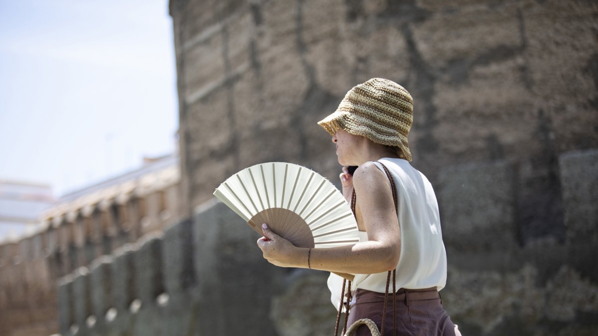 Una mujer se protege del sol con sombrero y abanico.