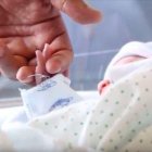 Un bebé recién nacido coge la mano de uno de sus padres.